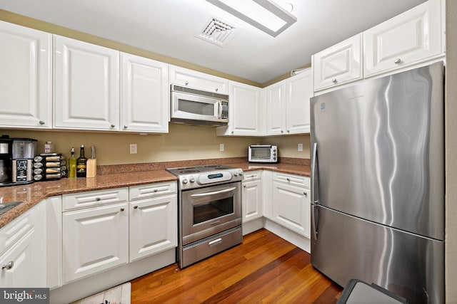 kitchen featuring white cabinets, appliances with stainless steel finishes, dark wood-type flooring, and dark stone countertops