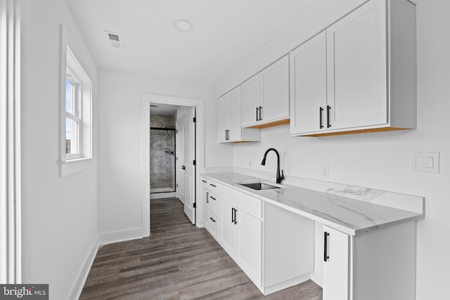 kitchen with light stone countertops, dark hardwood / wood-style flooring, white cabinetry, and sink