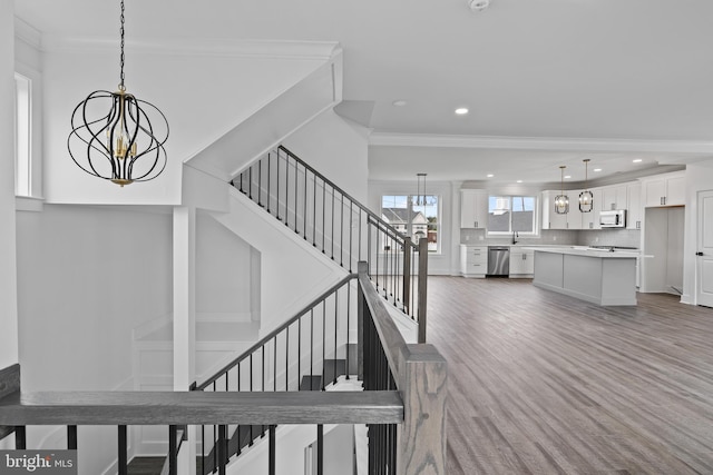 staircase with recessed lighting, crown molding, an inviting chandelier, and wood finished floors