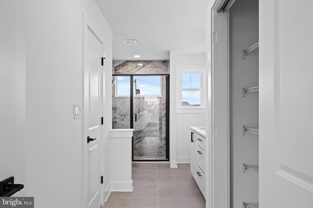 bathroom with visible vents, a walk in closet, baseboards, a stall shower, and vanity