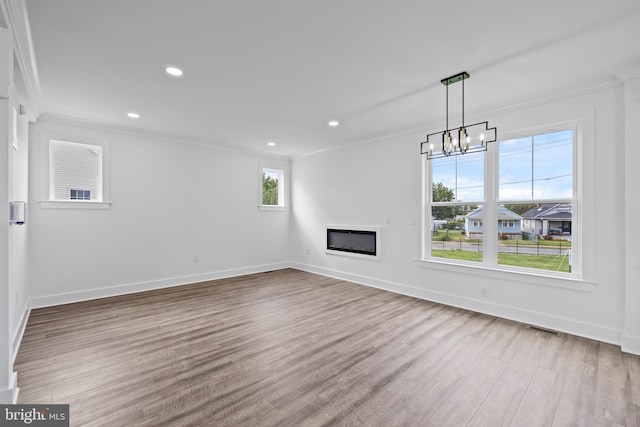 unfurnished living room with visible vents, wood finished floors, baseboards, and ornamental molding