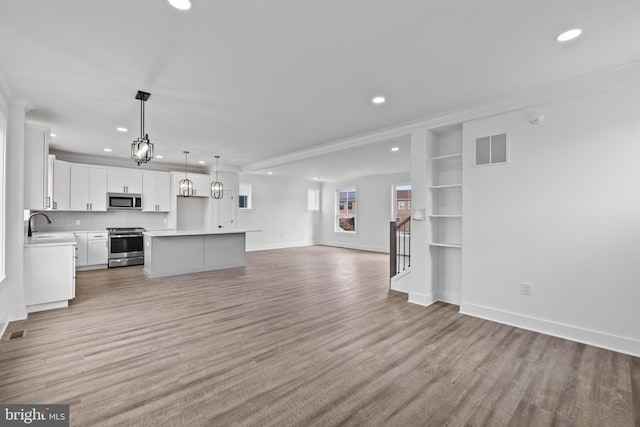 unfurnished living room featuring baseboards, visible vents, light wood finished floors, recessed lighting, and ornamental molding