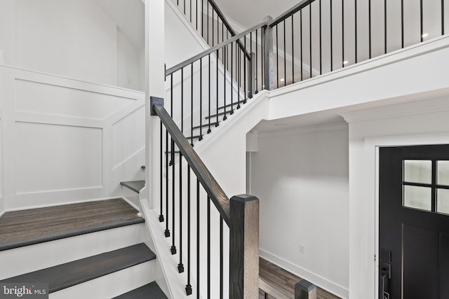 stairway with a towering ceiling, baseboards, and wood finished floors