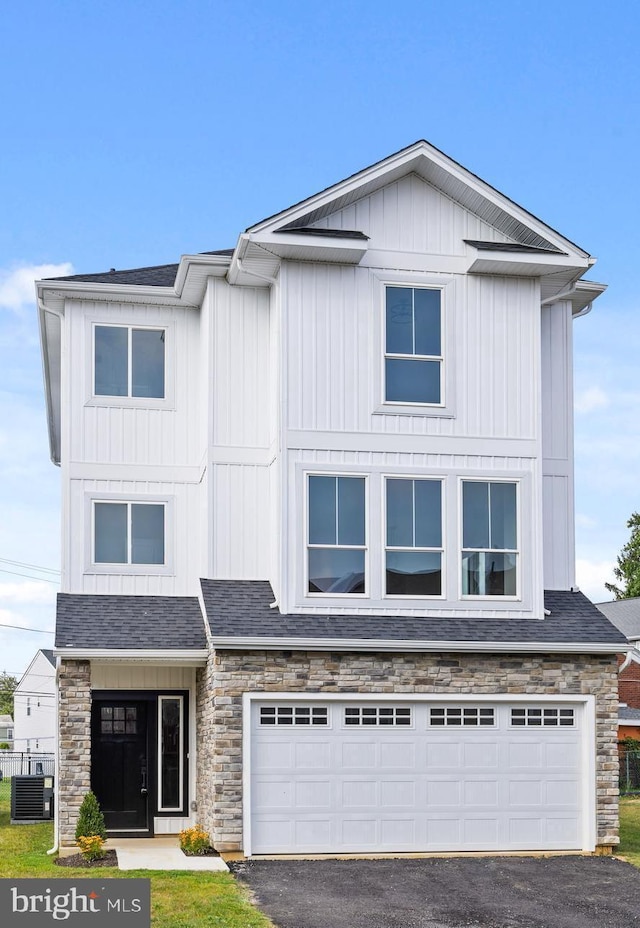 view of front of home with aphalt driveway, roof with shingles, cooling unit, stone siding, and an attached garage