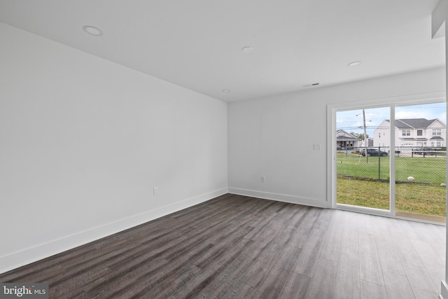 unfurnished room featuring a residential view, baseboards, visible vents, and dark wood finished floors