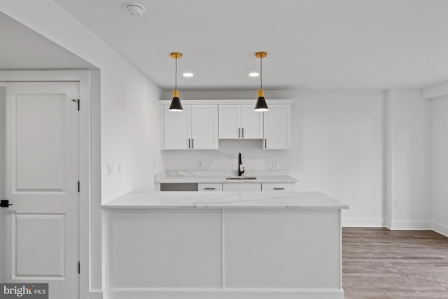 kitchen featuring light stone counters, wood finished floors, a sink, pendant lighting, and white cabinetry