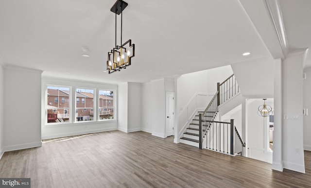 unfurnished living room featuring an inviting chandelier, crown molding, wood finished floors, and baseboards