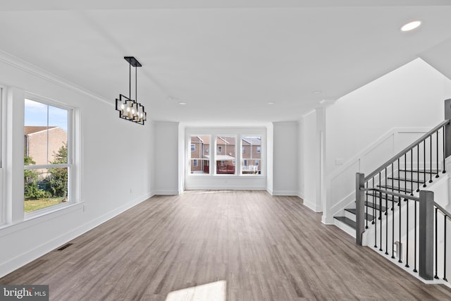 unfurnished living room featuring crown molding, light hardwood / wood-style floors, and a notable chandelier