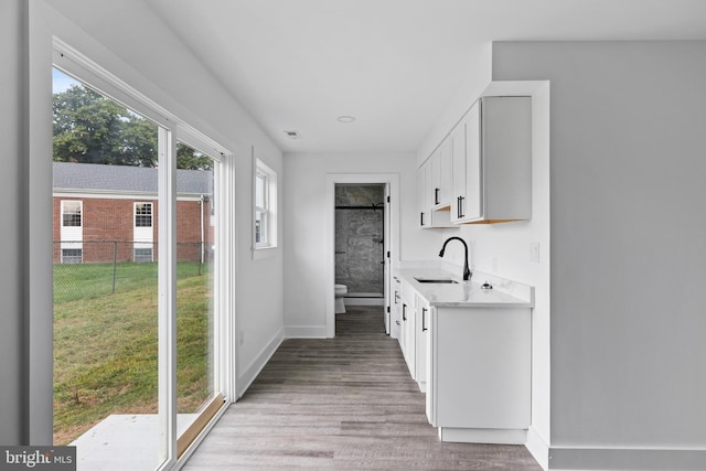 interior space featuring visible vents, baseboards, light wood-type flooring, white cabinetry, and a sink