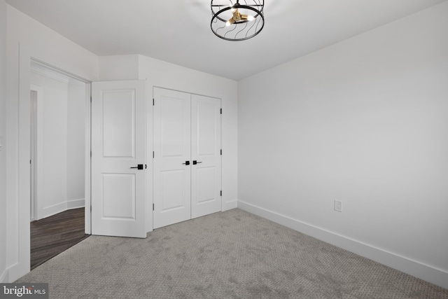 unfurnished bedroom featuring a closet, baseboards, carpet, and an inviting chandelier