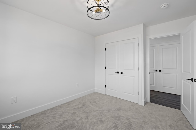 unfurnished bedroom with a closet, baseboards, carpet, and a chandelier