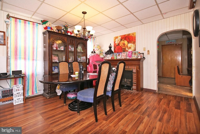 dining area featuring a fireplace, a drop ceiling, dark hardwood / wood-style floors, and an inviting chandelier