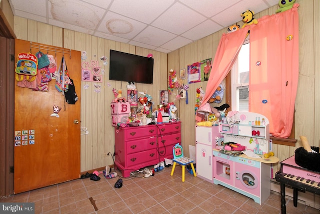 playroom featuring tile patterned floors, wood walls, and a drop ceiling