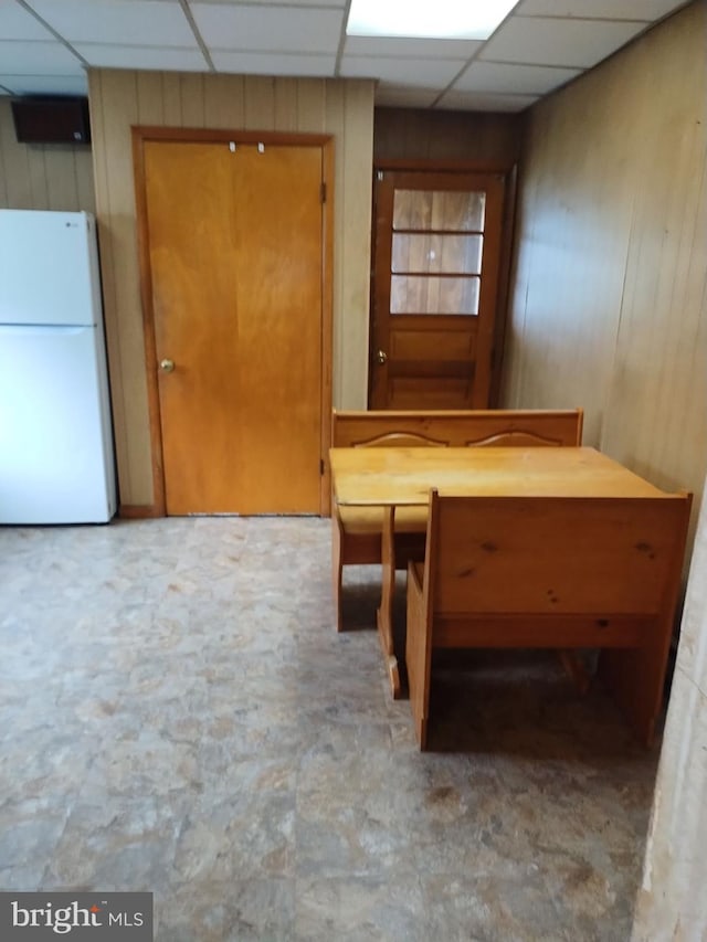 unfurnished dining area with a paneled ceiling and wood walls