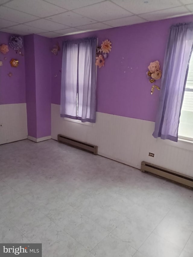 empty room featuring a paneled ceiling and a baseboard heating unit