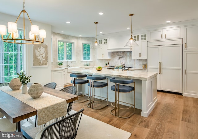 kitchen featuring premium range hood, paneled fridge, white cabinetry, light hardwood / wood-style floors, and a kitchen island