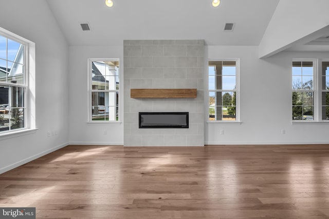 unfurnished living room with wood-type flooring, vaulted ceiling, and a tiled fireplace