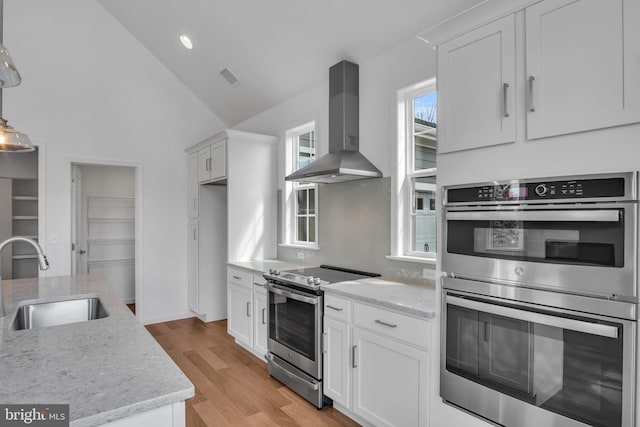 kitchen featuring appliances with stainless steel finishes, tasteful backsplash, wall chimney exhaust hood, sink, and white cabinetry