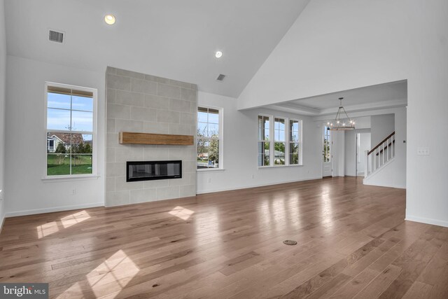 unfurnished living room with high vaulted ceiling, wood-type flooring, a tile fireplace, and a chandelier