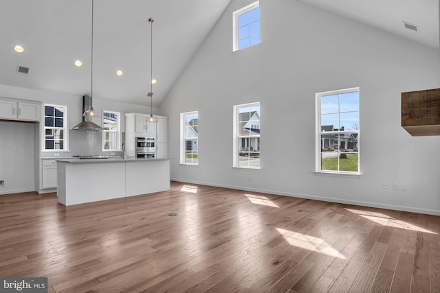 unfurnished living room with sink, a high ceiling, and light hardwood / wood-style flooring