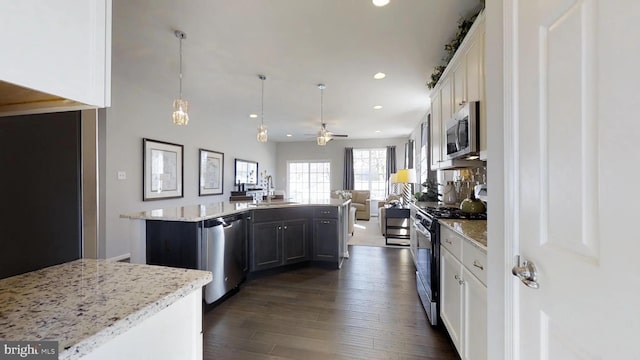 kitchen featuring a center island with sink, ceiling fan, appliances with stainless steel finishes, decorative light fixtures, and white cabinetry