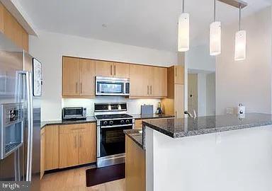 kitchen with pendant lighting, dark stone counters, light hardwood / wood-style floors, kitchen peninsula, and stainless steel appliances