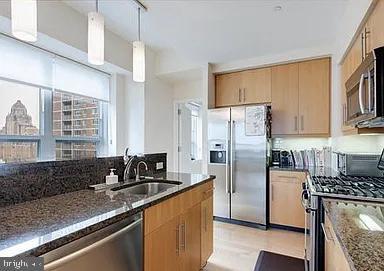 kitchen featuring track lighting, hanging light fixtures, sink, dark stone countertops, and appliances with stainless steel finishes