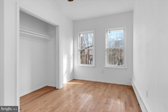 unfurnished bedroom with light hardwood / wood-style floors, a closet, and a baseboard heating unit