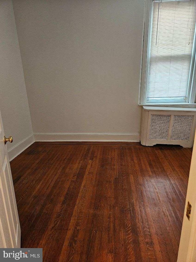 unfurnished room with dark hardwood / wood-style flooring and radiator