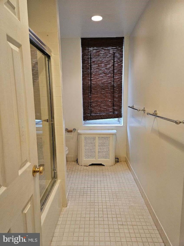 bathroom featuring tile patterned flooring, combined bath / shower with glass door, toilet, and radiator