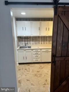 bar featuring a barn door, white cabinetry, and sink