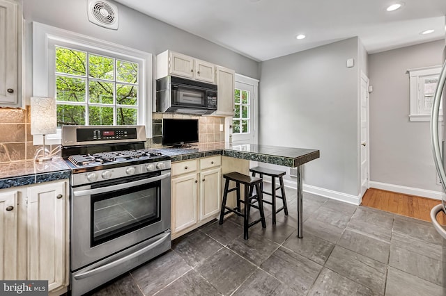 kitchen with tile counters, stainless steel gas range oven, black microwave, and a healthy amount of sunlight