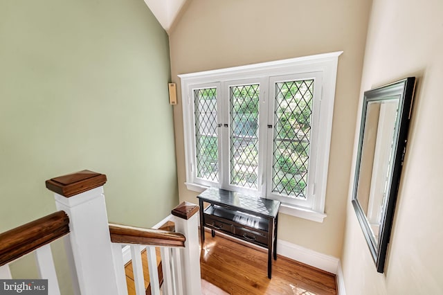 staircase with baseboards, lofted ceiling, wood finished floors, and a wealth of natural light