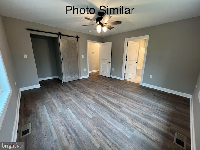 unfurnished bedroom featuring a barn door, ensuite bathroom, ceiling fan, and wood-type flooring