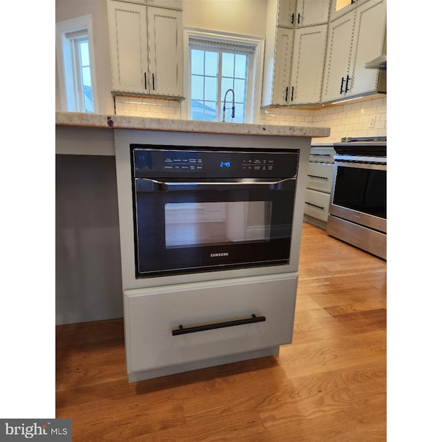 kitchen featuring stainless steel range, white cabinets, light hardwood / wood-style floors, oven, and decorative backsplash