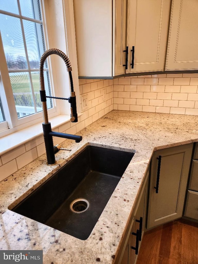 kitchen with sink, wood-type flooring, decorative backsplash, and light stone countertops