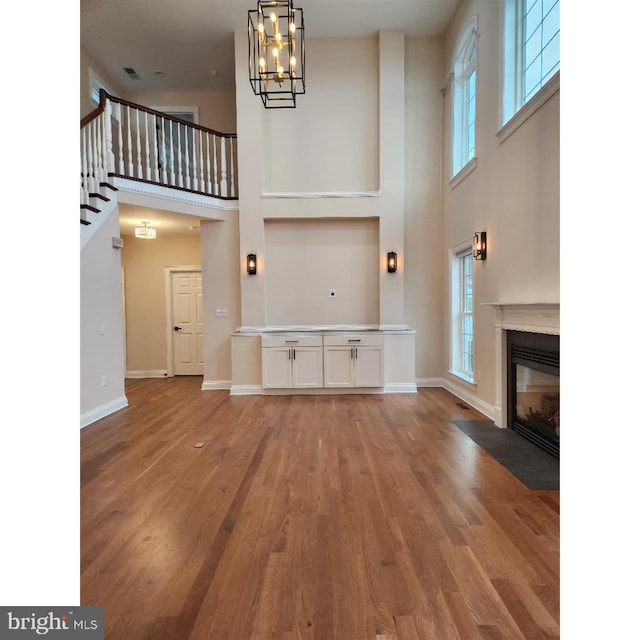 unfurnished living room with an inviting chandelier, hardwood / wood-style flooring, and a towering ceiling