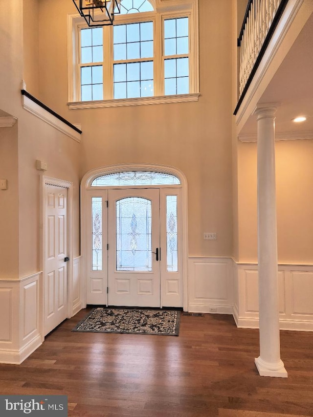 entrance foyer featuring decorative columns, crown molding, a towering ceiling, and dark wood-type flooring