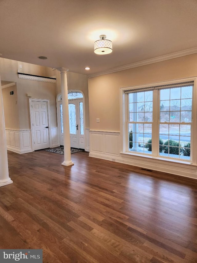 unfurnished living room featuring ornate columns, a wealth of natural light, and dark wood-type flooring