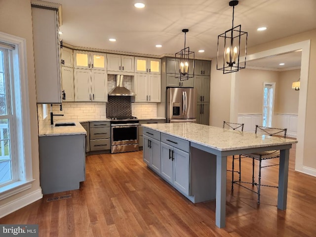 kitchen with wood-type flooring, wall chimney range hood, stainless steel refrigerator with ice dispenser, stove, and a kitchen island