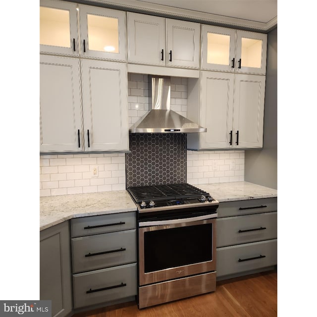 kitchen with tasteful backsplash, wall chimney range hood, hardwood / wood-style flooring, stainless steel gas range, and gray cabinetry