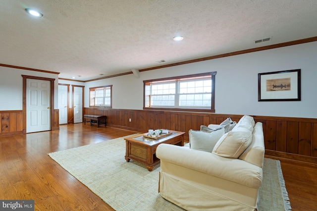 living room with crown molding, hardwood / wood-style floors, a textured ceiling, and wooden walls