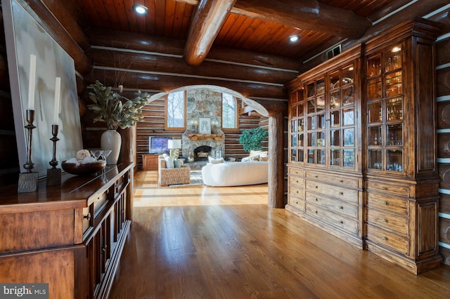 interior space with wood ceiling, log walls, beam ceiling, wood-type flooring, and a stone fireplace