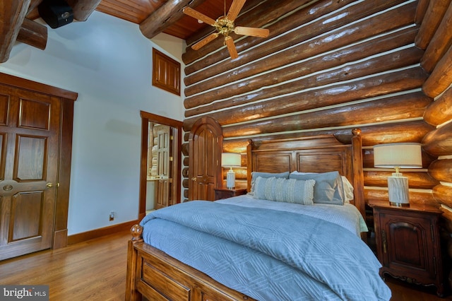 bedroom featuring ceiling fan, log walls, light hardwood / wood-style flooring, wooden ceiling, and beamed ceiling