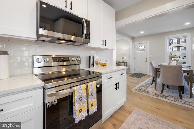 kitchen with light stone countertops, appliances with stainless steel finishes, light wood-type flooring, and white cabinetry