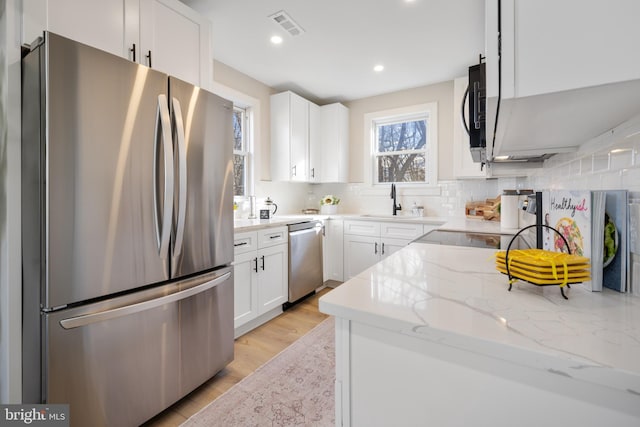 kitchen featuring sink, light stone counters, backsplash, white cabinets, and appliances with stainless steel finishes