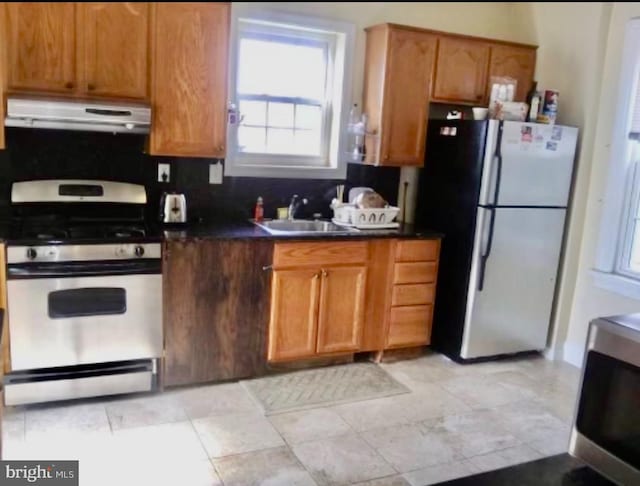 kitchen with light tile floors, gas range, stainless steel refrigerator, and sink