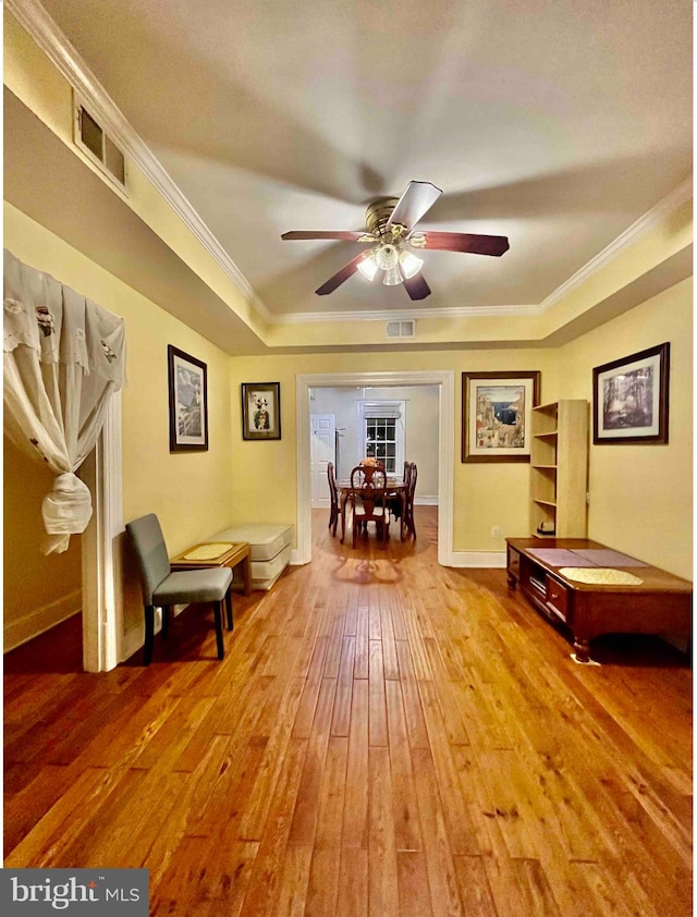 sitting room with ceiling fan, ornamental molding, a tray ceiling, and wood-type flooring