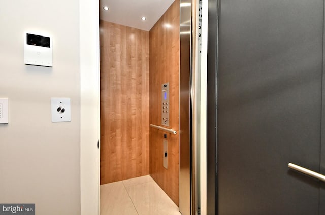 bathroom with tile patterned floors, elevator, and wooden walls