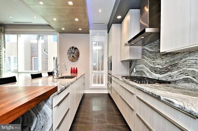 kitchen with decorative backsplash, light stone counters, wall chimney exhaust hood, stainless steel appliances, and sink